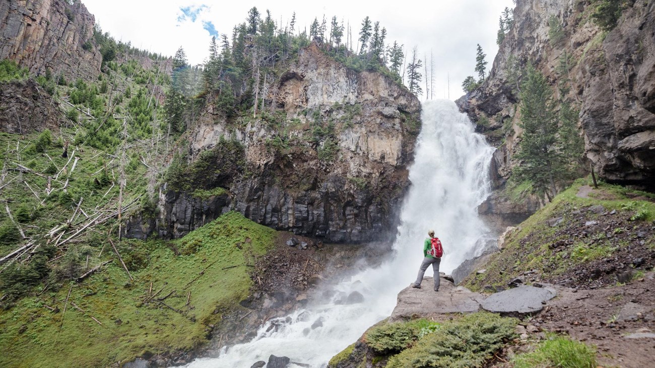 A hiker stands at the base of a large waterfall.