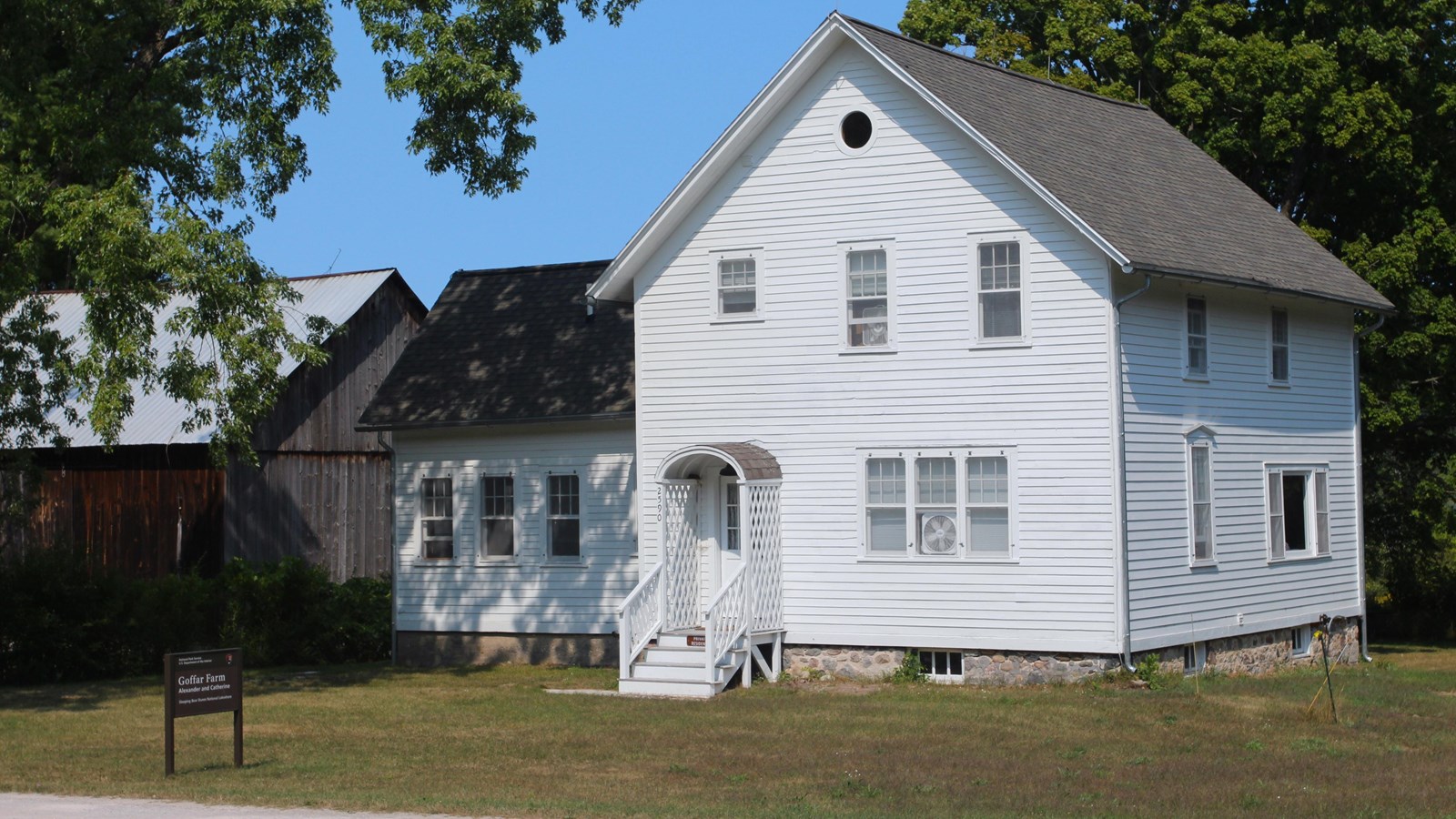 A white farmhouse along side a road with a barn in the background