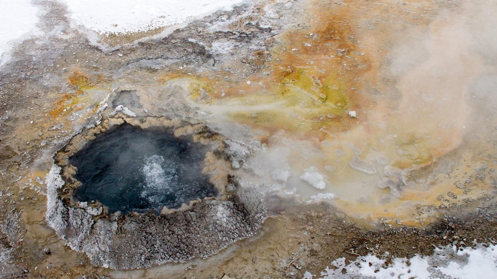 A small hot spring surrounded by a cone of sinter bubbles and releases steam.