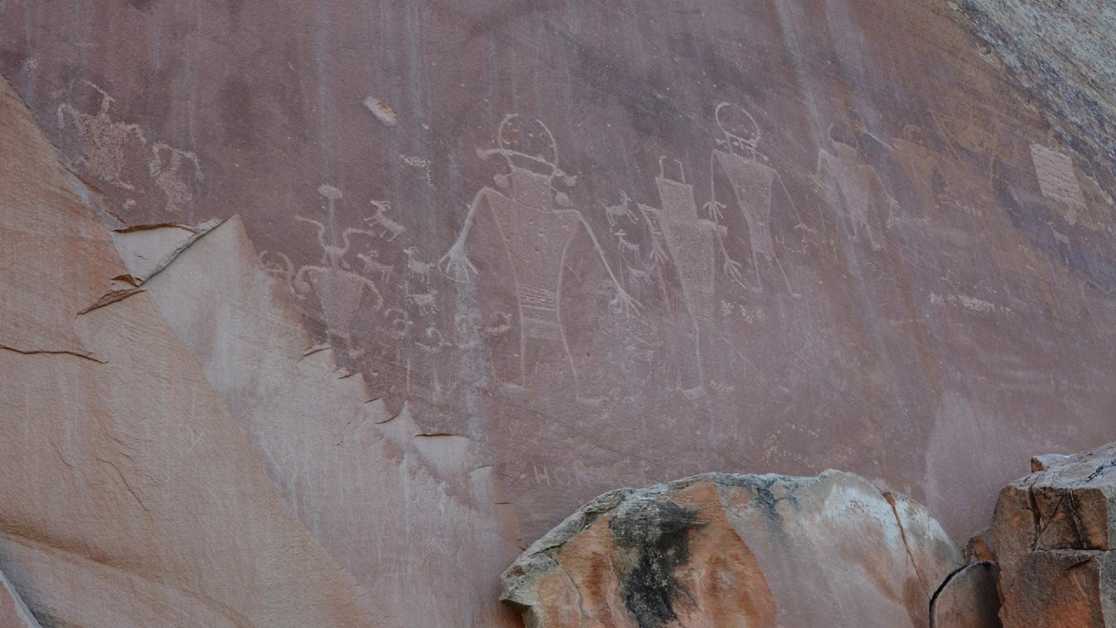 Rock markings carved into flat red rock depicting human-like figures with trapezoidal bodies.