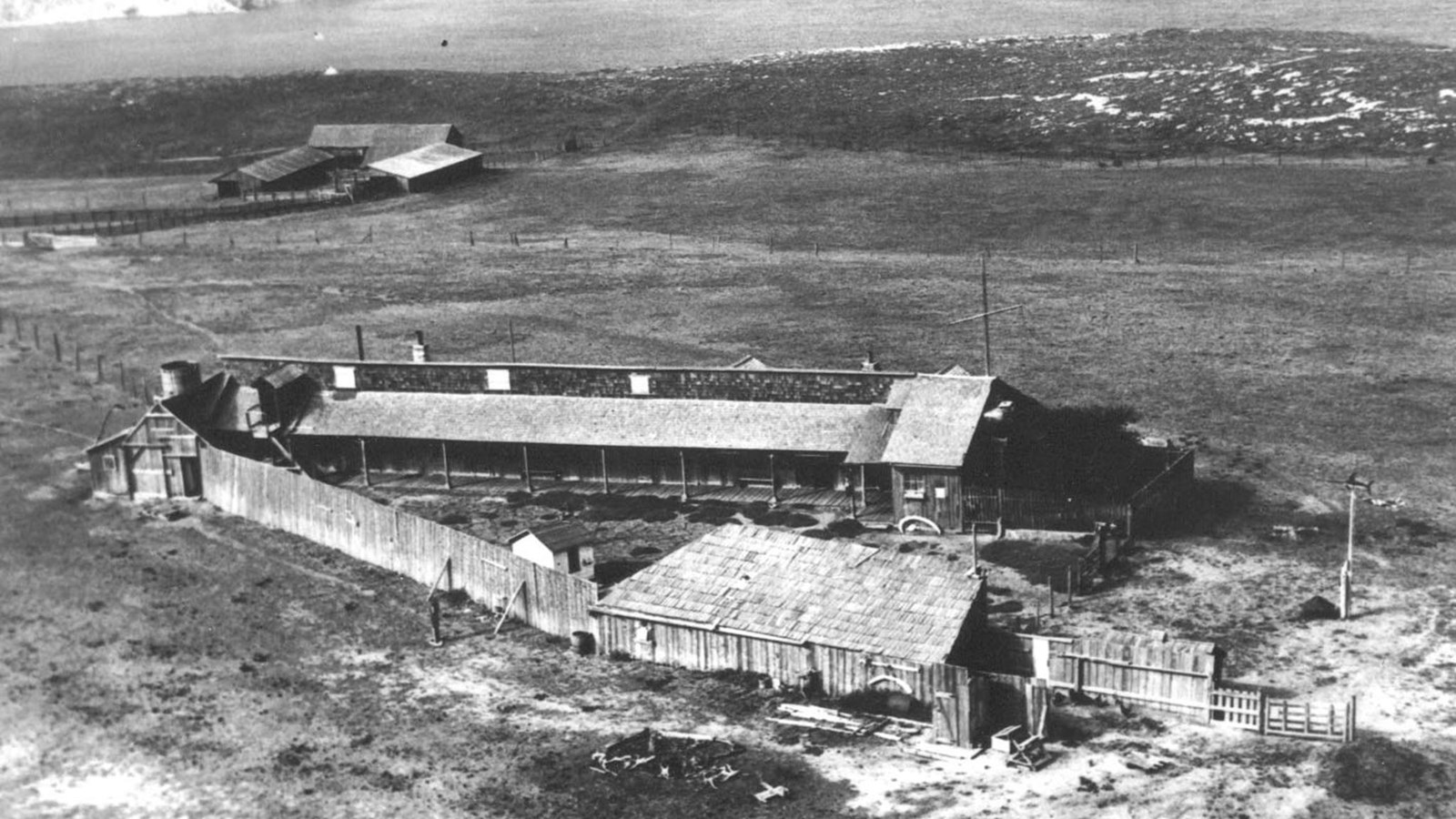ranch house with fence in v-shaped formation with barn in background overlooking harbor.