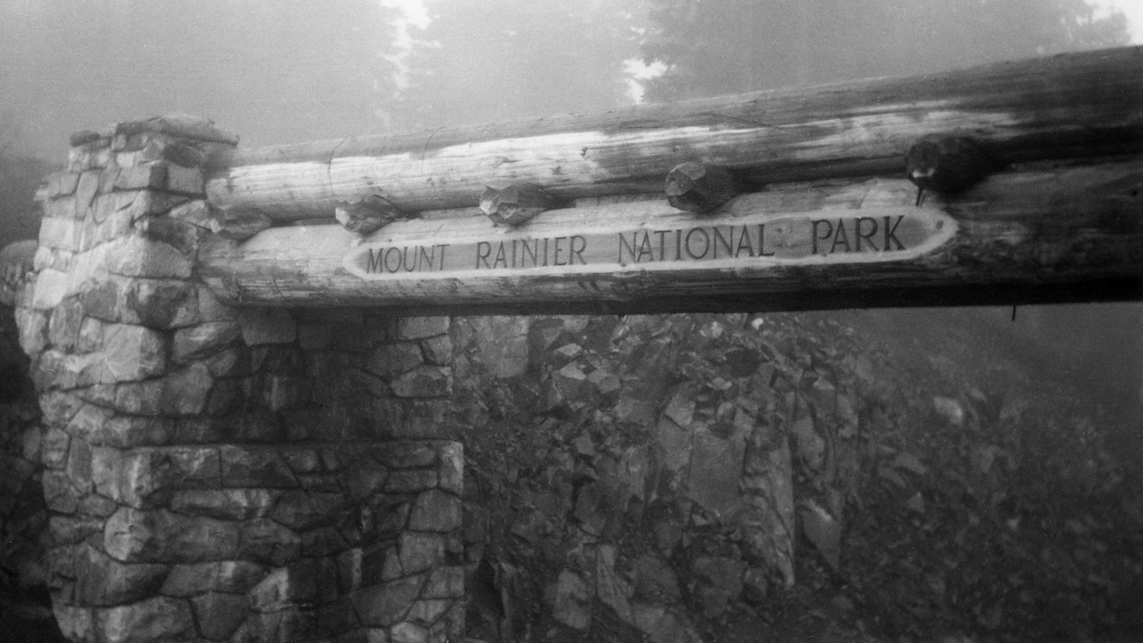 A black and white photo of a log bridge with stone abutments. 