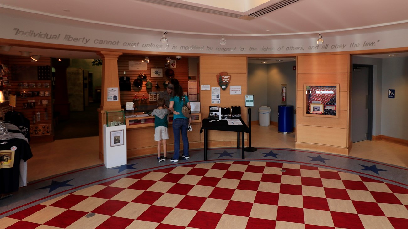 A woman and a child stand at a desk with a ranger behind the counter