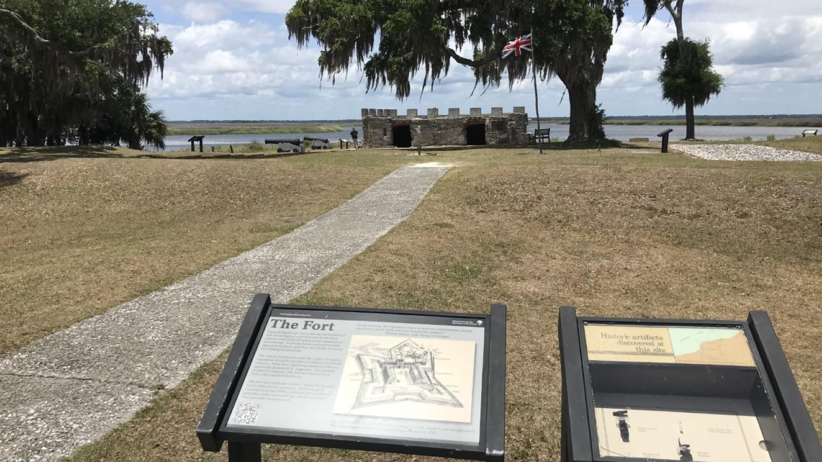 Wayside with text overlooking the fortification remains with grassy area between and river behind.