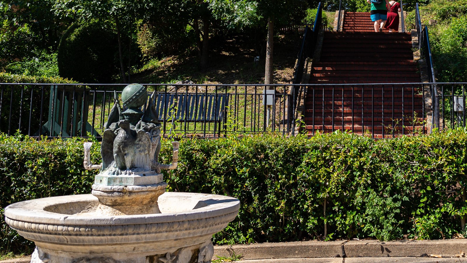 A stone fountain with two iron eagles sitting atop a globe, next to a staircase leading to a trail.