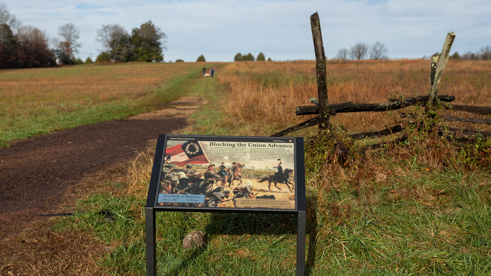 An informational panel in front of a wooden fence and a trail. 