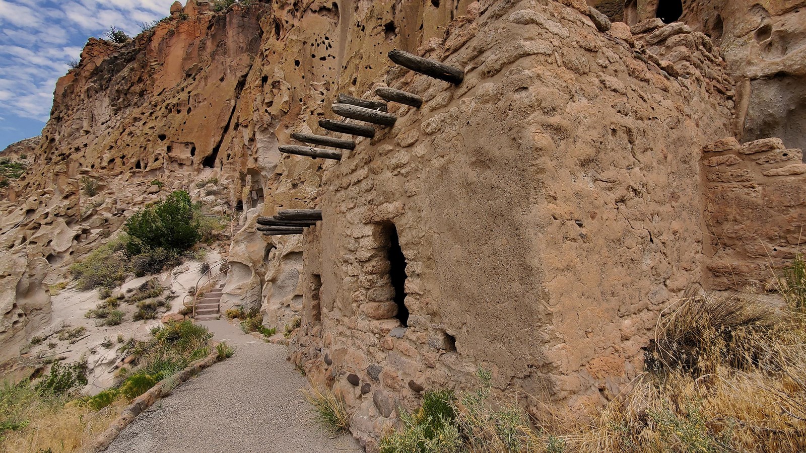 A stone structure has jutting roof supports and an open window into the interior with a clouded sky