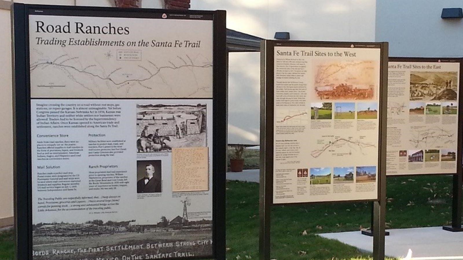 Three standing exhibits about the Santa Fe Trail in a grassy yard