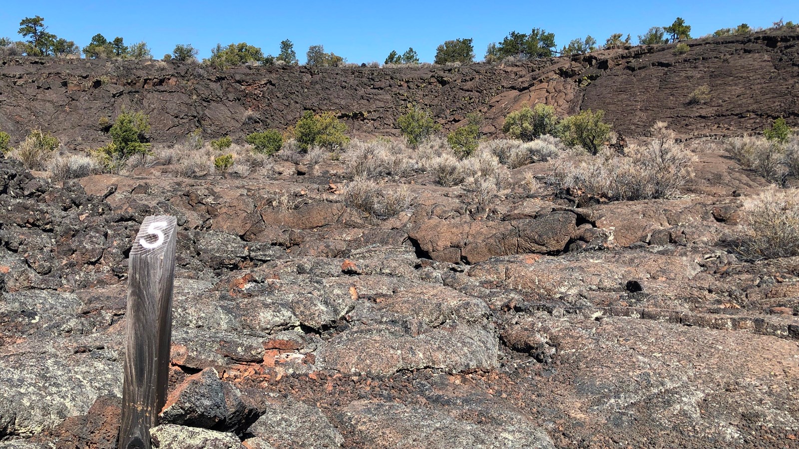 A wood post with a painted number 5 is surrounded by nearby ridges of lava rock.