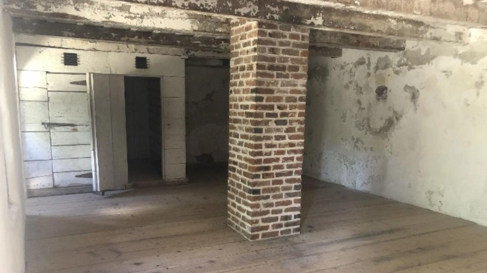 A brick pillar in the center of small white room with blank walls