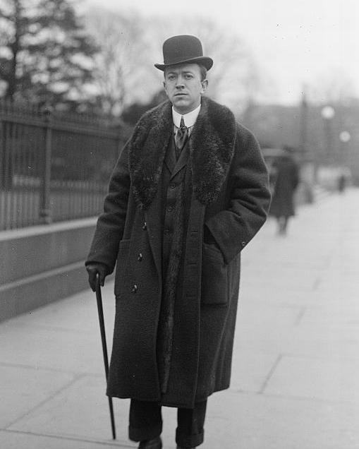 a man in a bowler hat and trench coat is walking along a sidewalk