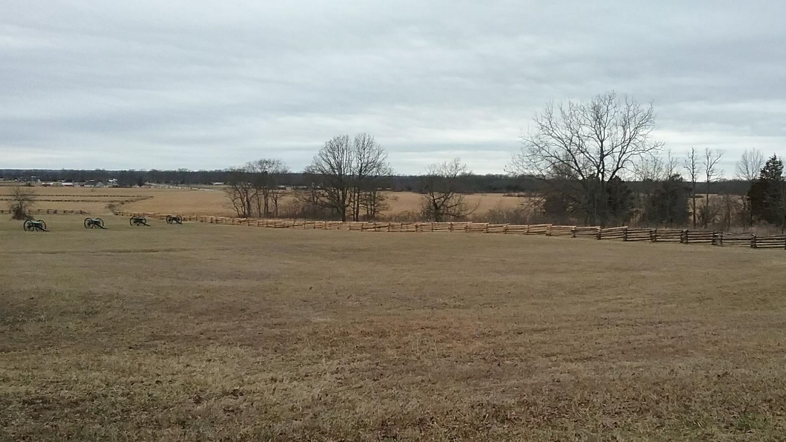 Photo of grassy field with, split rail fences in the background with a shot line of tress