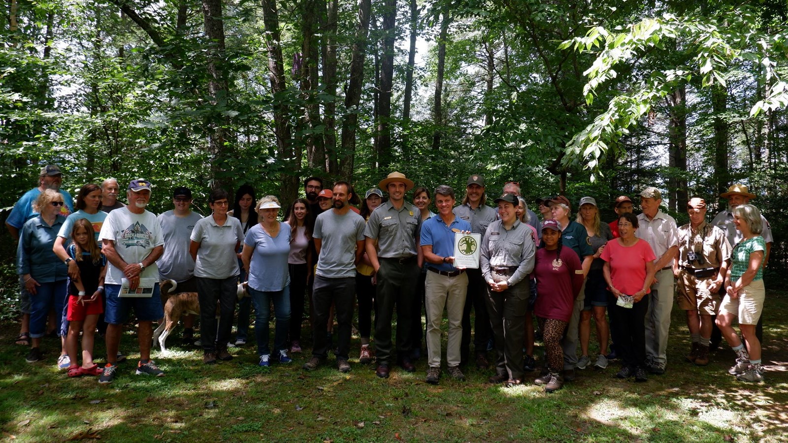 A group of 34 people with 3 park rangers posing in front of trees in a forest.