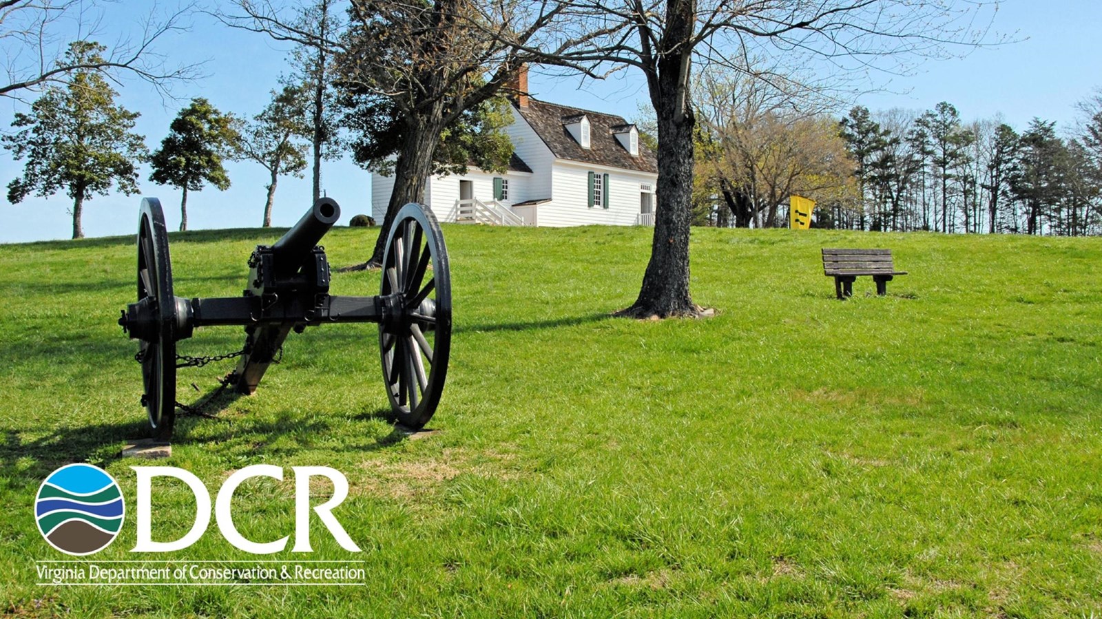 A historic site featuring a black cannon on green grass and a white under a blue sky. 