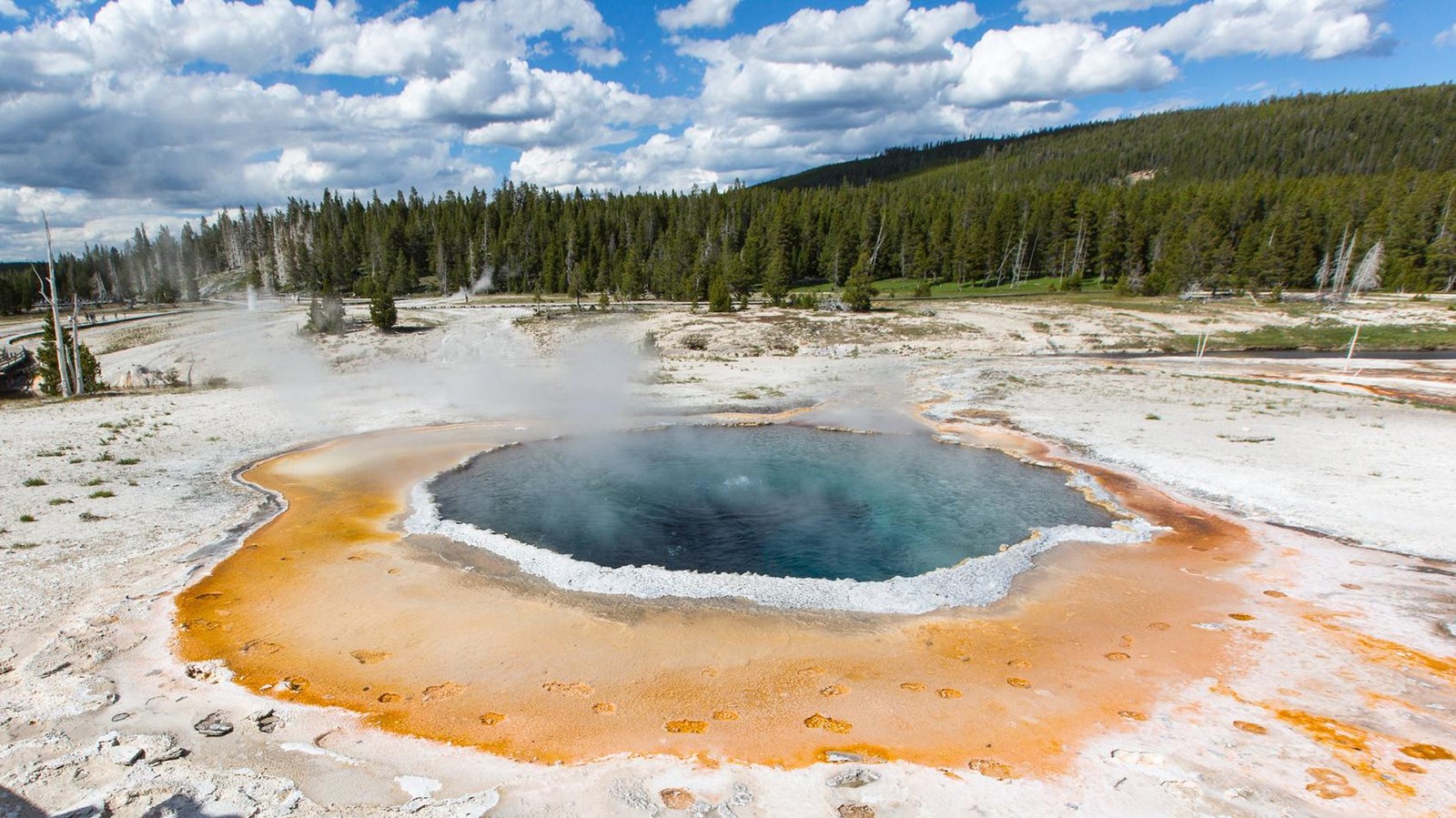 A deep blue hot spring surrounded by orange microbial mats.