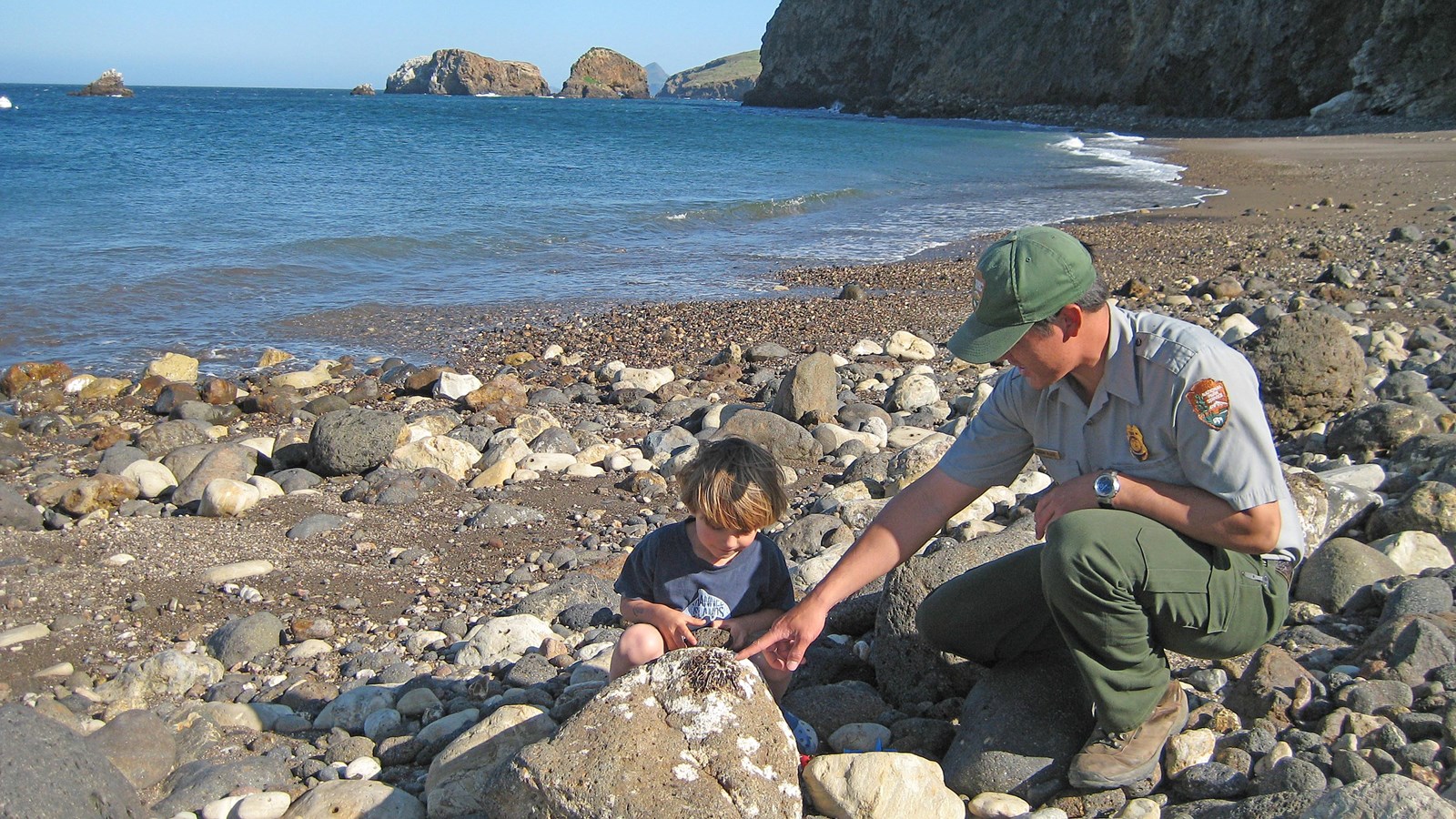 ranger with boy on beach looking at rocks.