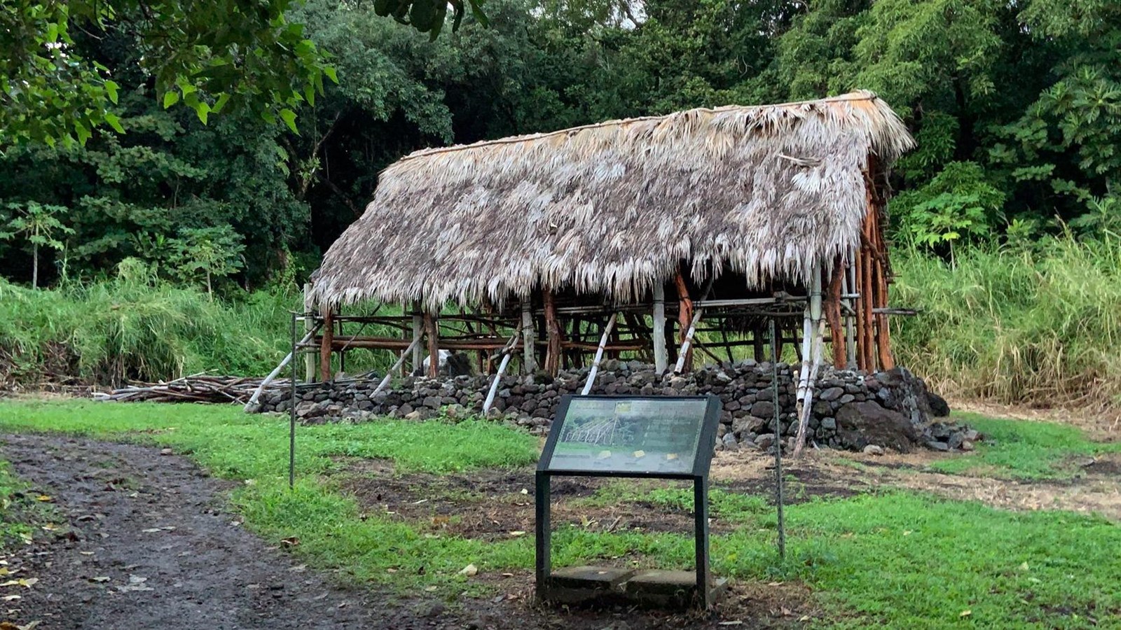 A traditional open air Hawaiian building stands upon a lava rock foundation.