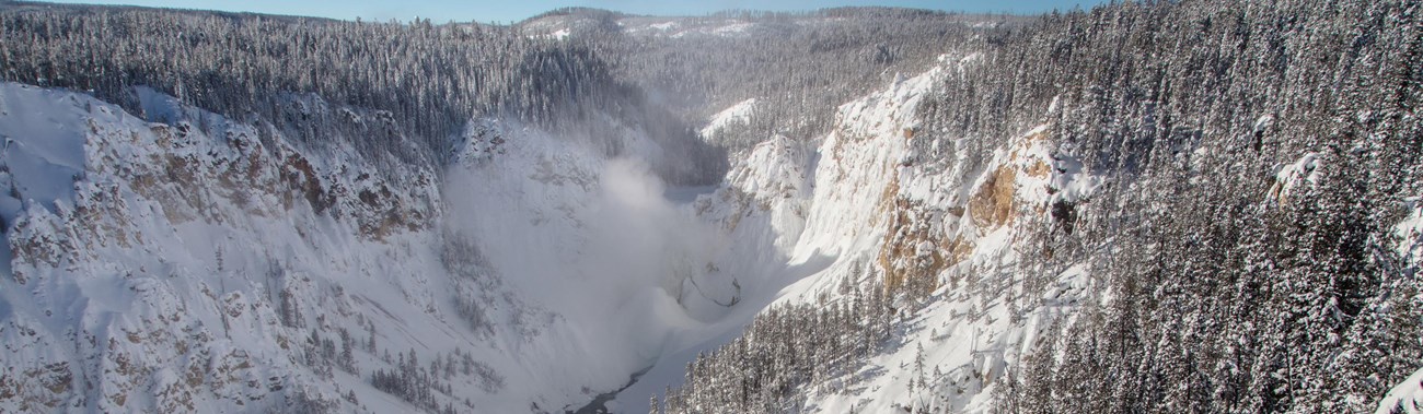Snow covers a deep canyon, with ice and mist covering the waterfall plunging down into the canyon.