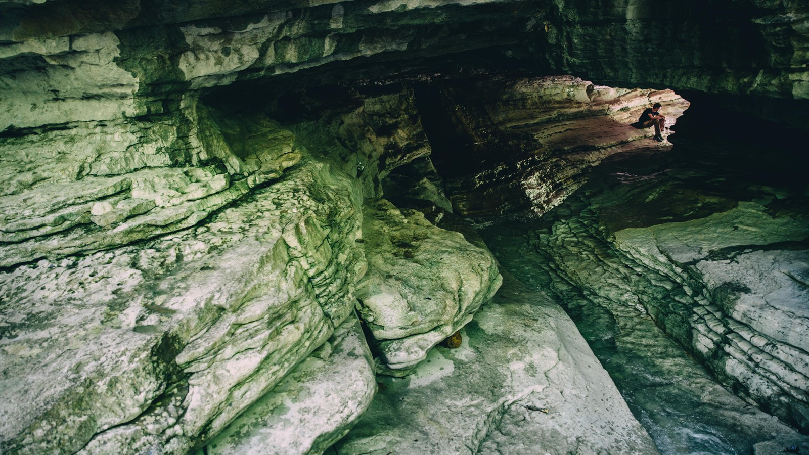 A 50-foot-long tunnel of limestone carved by Clark Creek and time. A hiker sits at the opposite end.