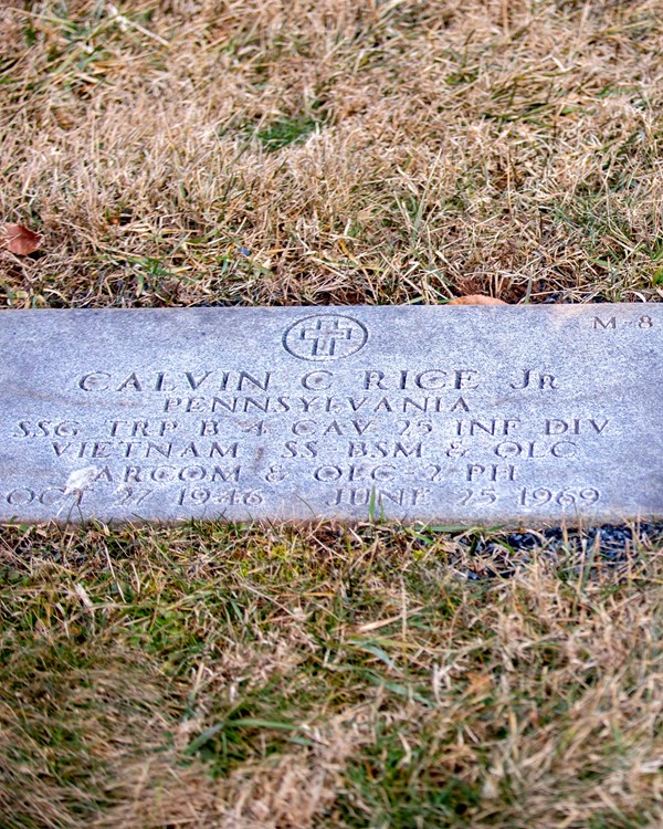 The gravestone of Calvin C. Rice Jr. is flat on the ground on the left next to a color photo of him.