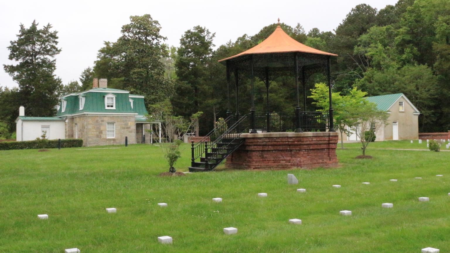A gazebo-like structure center; a lodge to the back left; foreground 3 rows of block headstones.