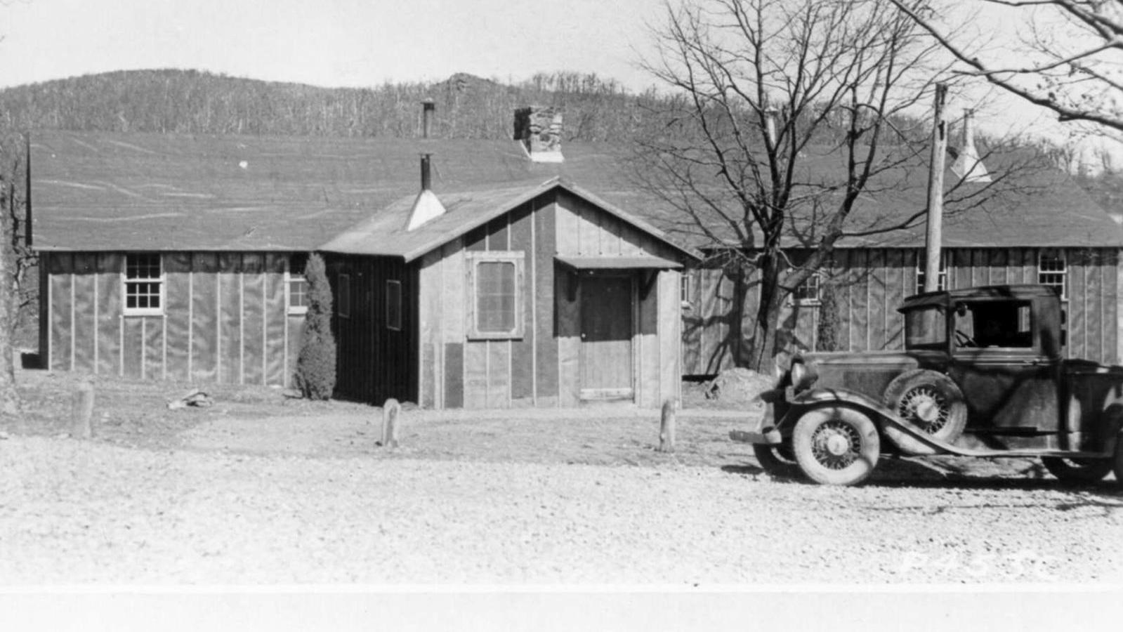 A long building with an L-on the front. A vehicle sits in front of it.