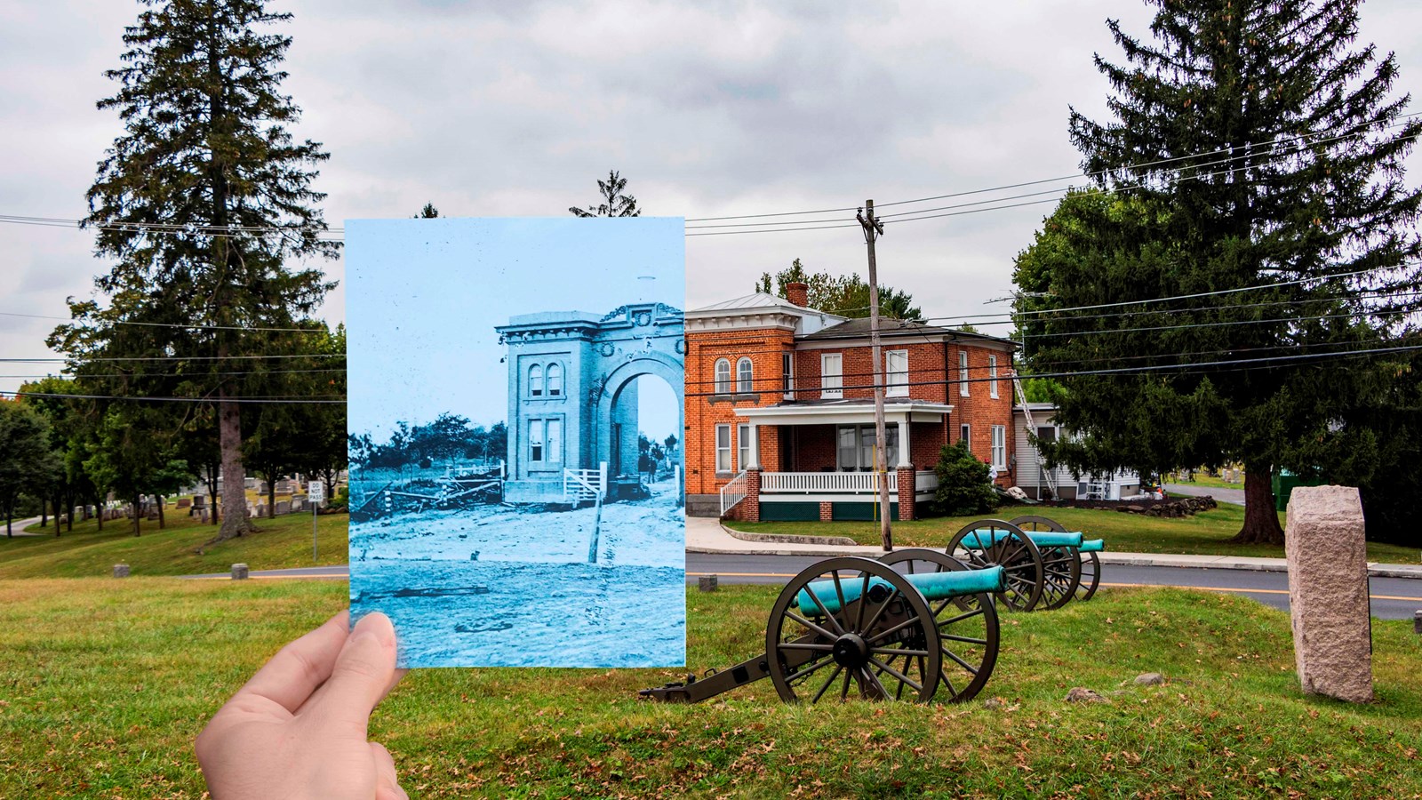 A tall brick building sits across a road with three cannons and a monument in front of it.