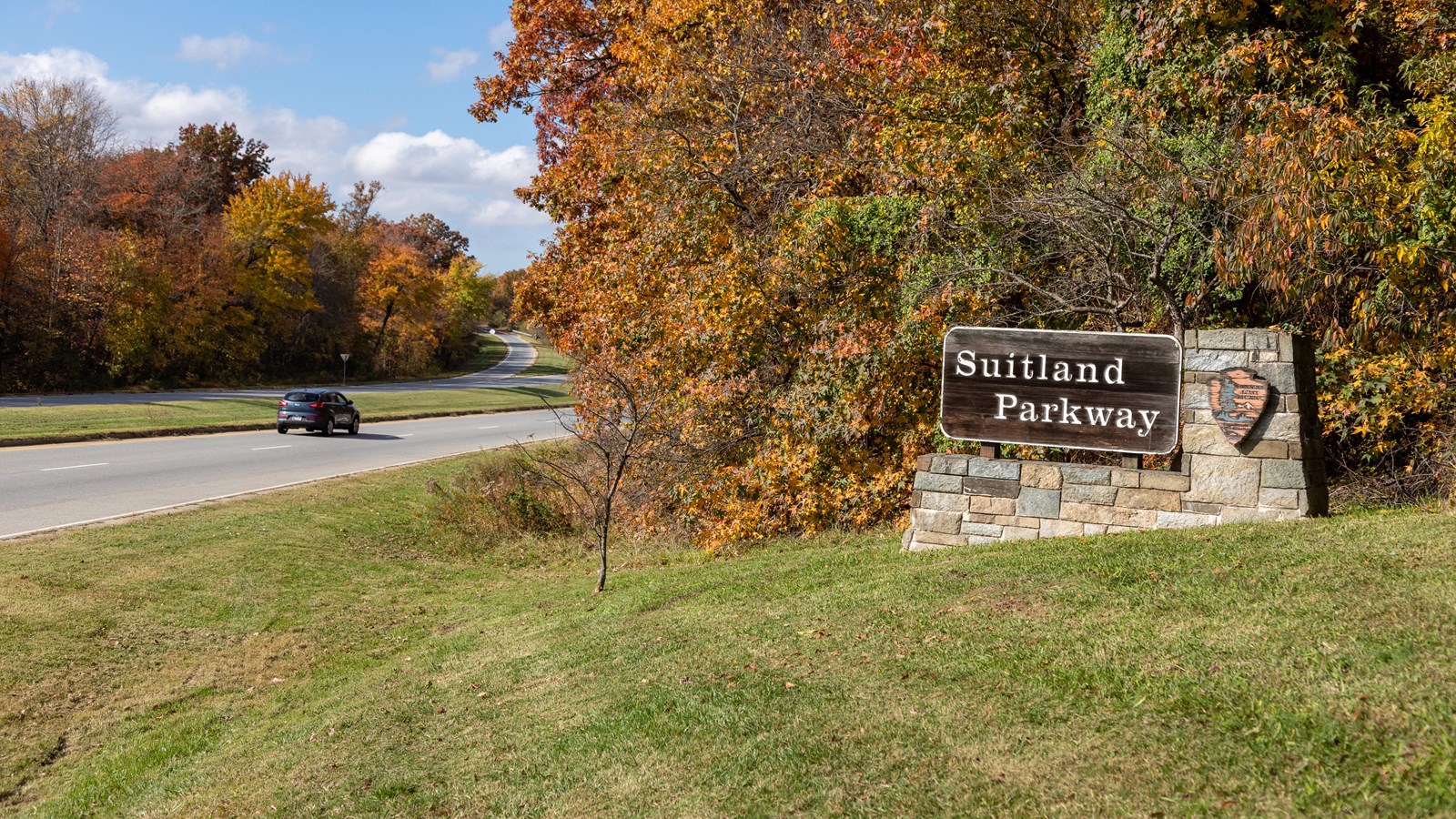 A brown sign that reads \'Suitland Parkway\' next to a two lane road with cars 