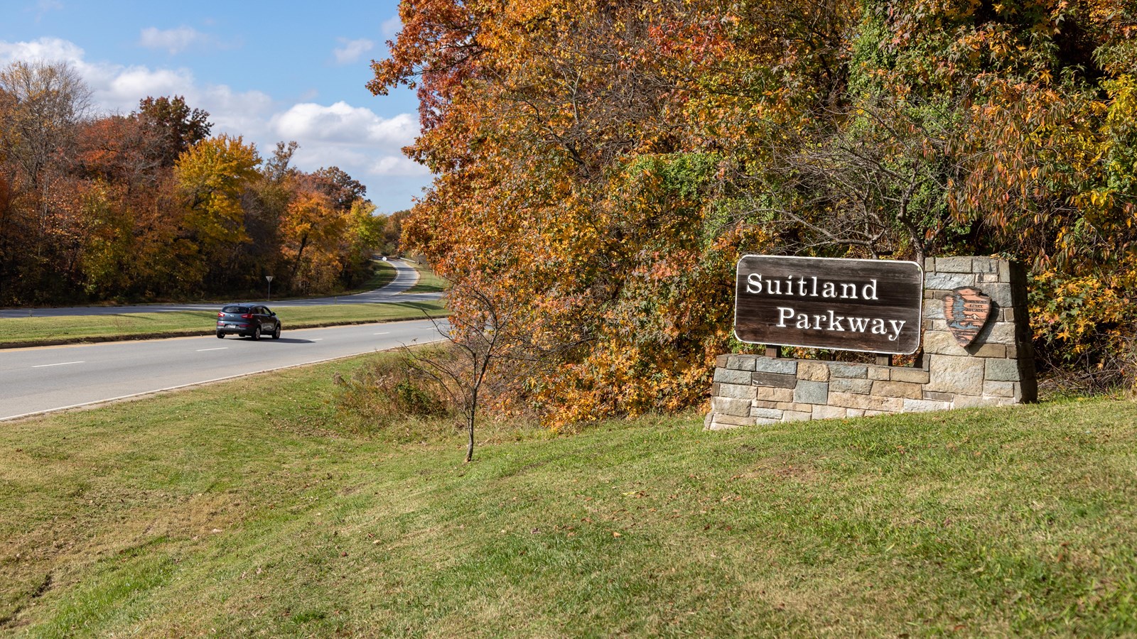 A brown sign that reads \'Suitland Parkway\' next to a two lane road with cars