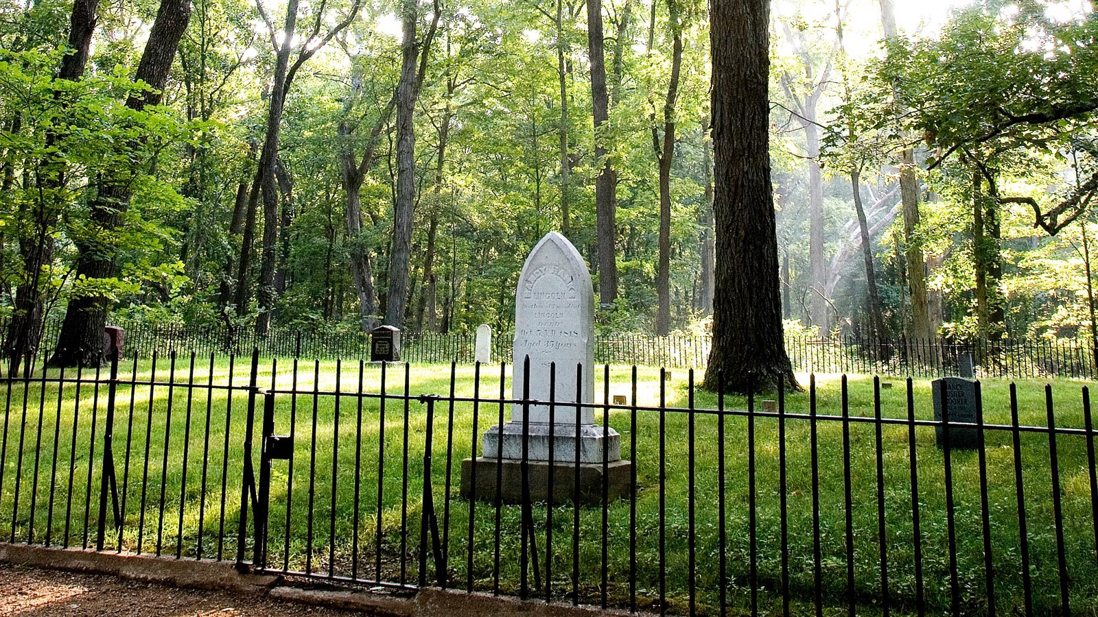 Cemetery with iron fence. Dappled light through trees.