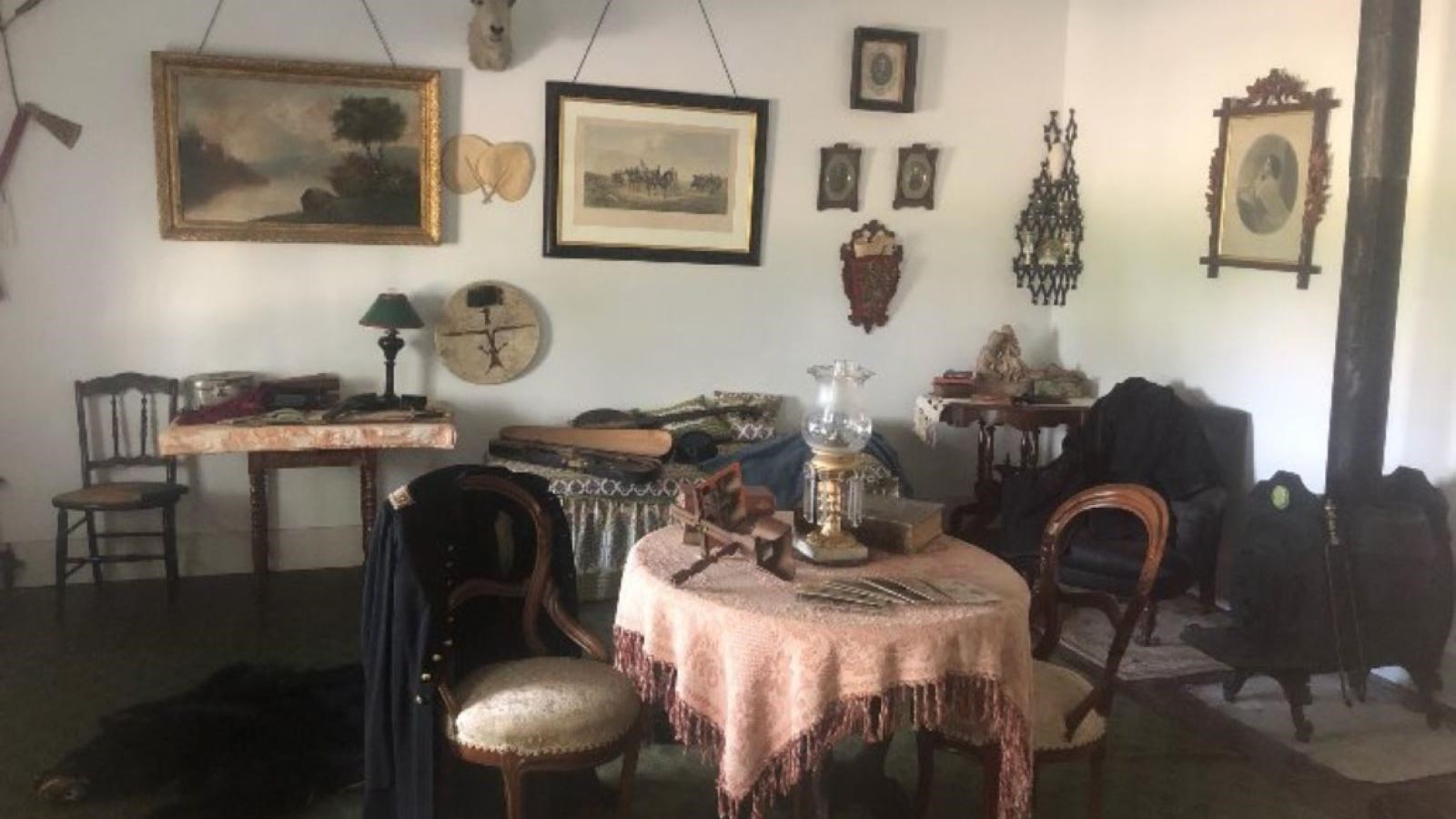 A room filled with paintings, a table with several chairs, and wood burning stove 