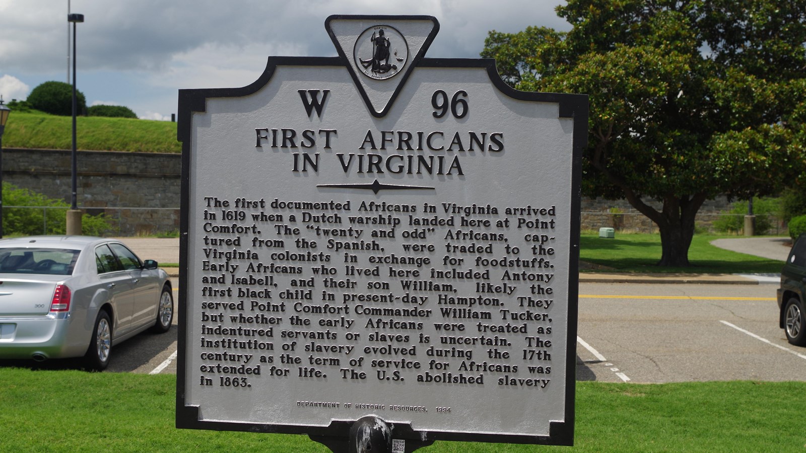 Historical Highway Marker standing in front of Fort Monroe under cloudy skies against green grass