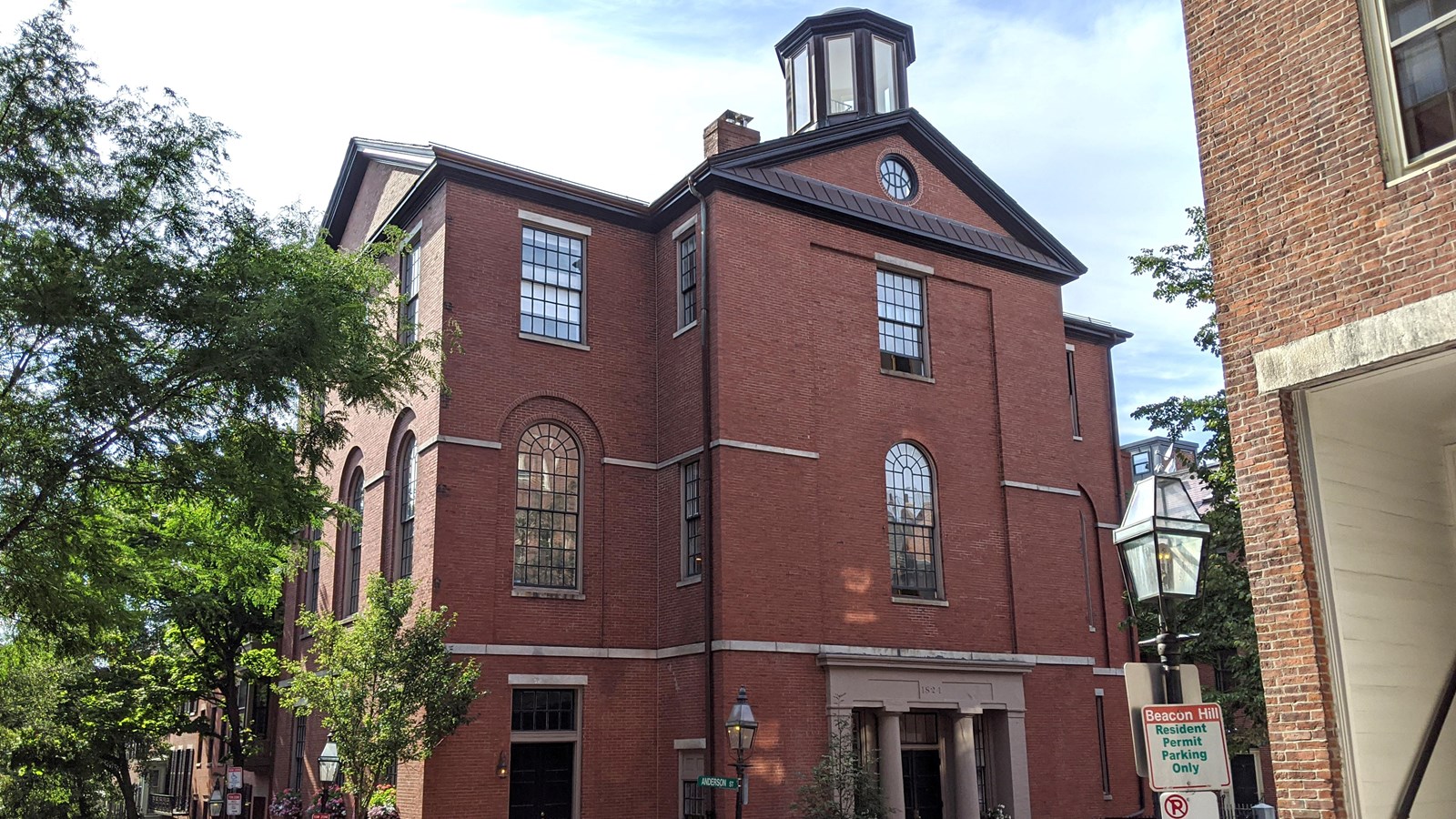 A four story red brick building on the corner of two streets with a small tower or cupola on top.