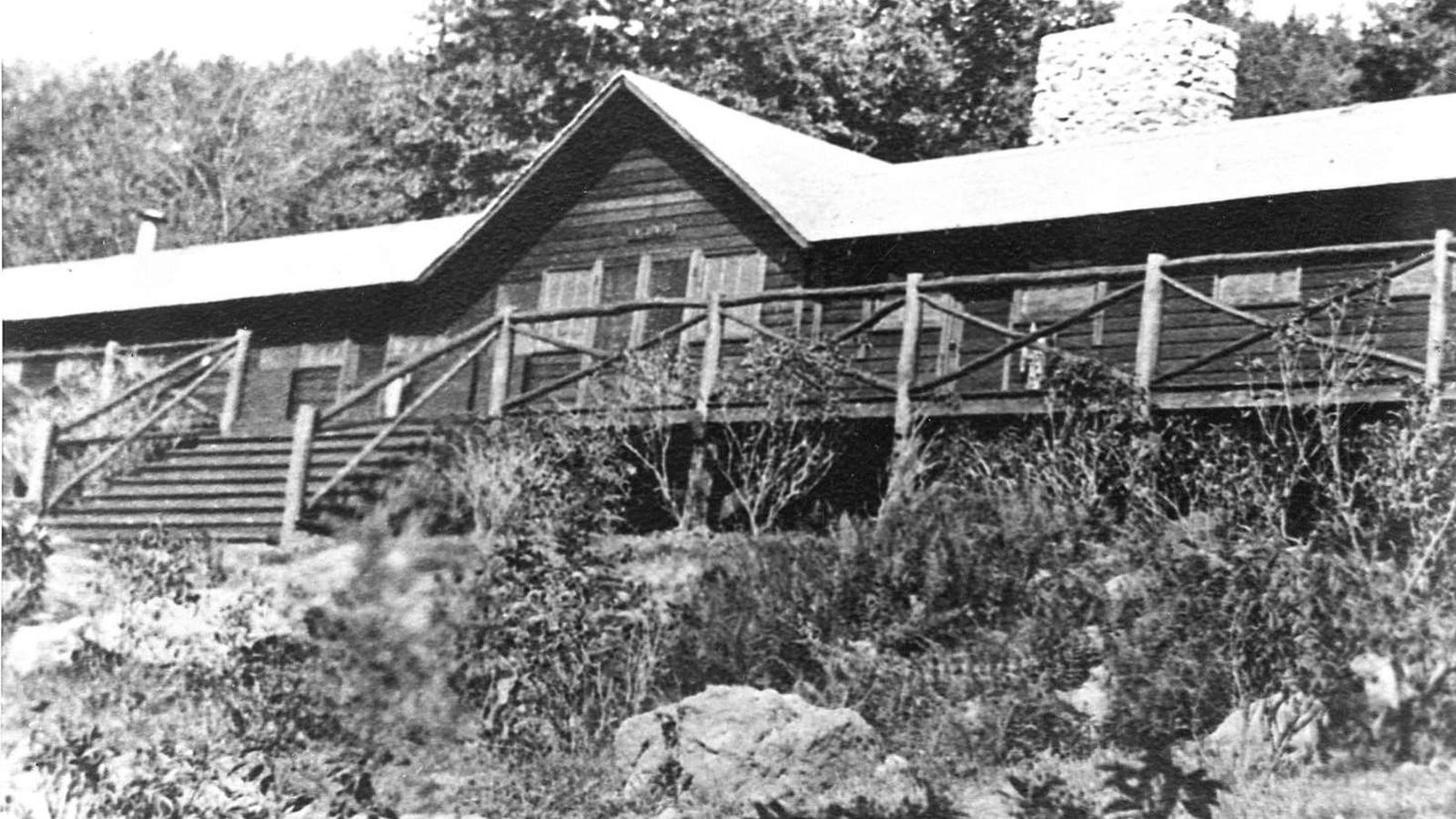 A long wood-sided structure with a large chimney just right of the gabled center.