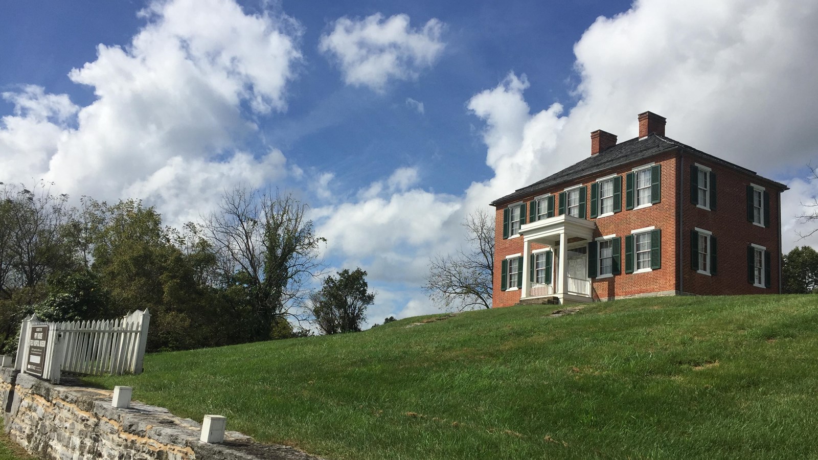 red brick house on hill with white fence surrounding the outside