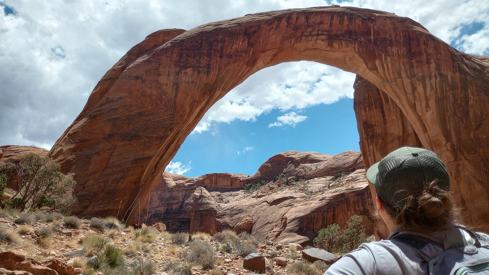 Park ranger has back to camera, looking at a perfect natural sandstone arch.