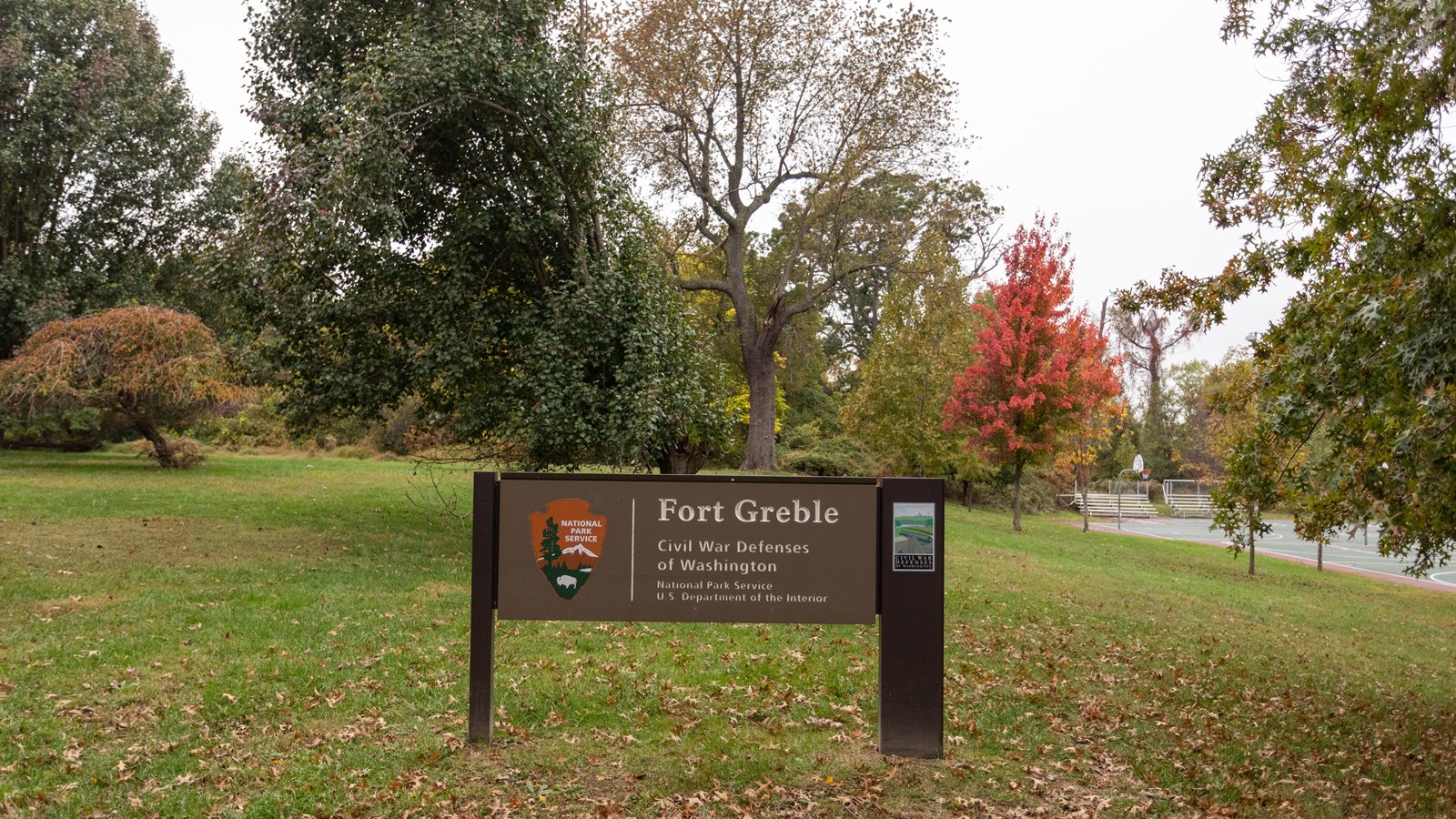 A large NPS sign in front of a grassy field and trees.
