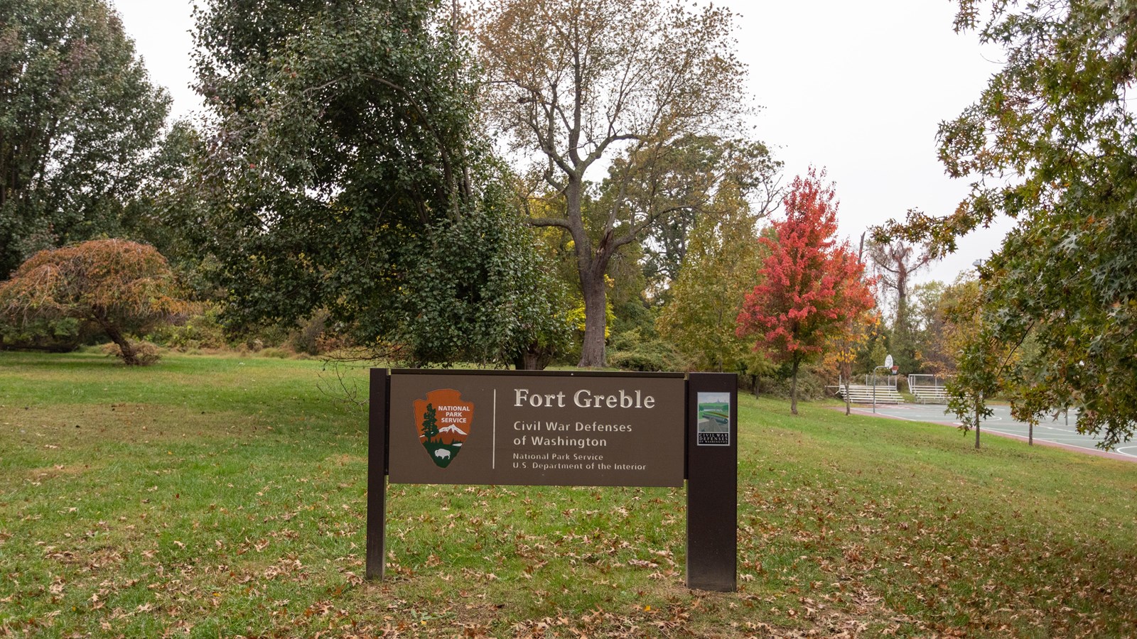 A large NPS sign in front of a grassy field and trees. 