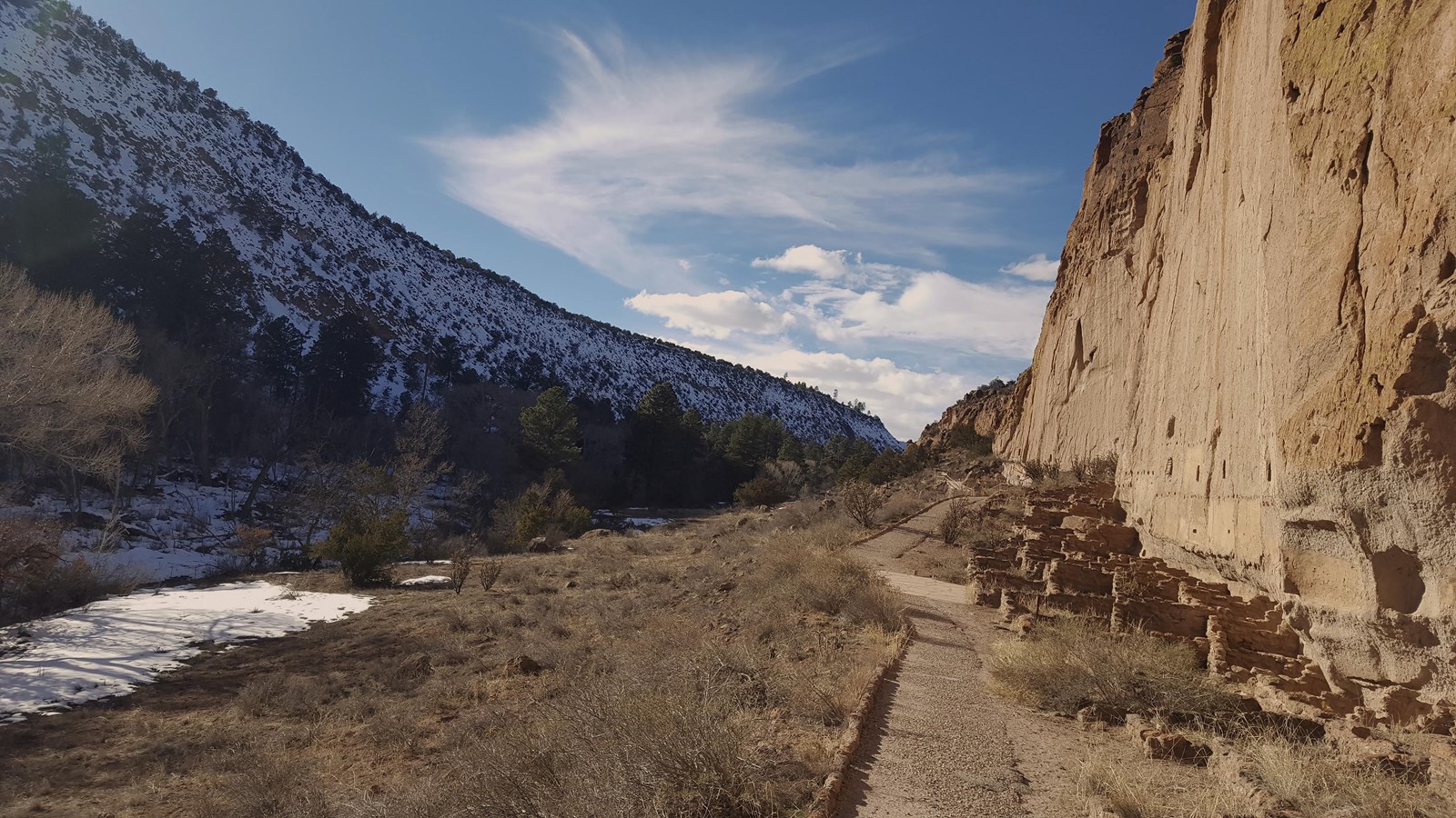 a stone wall with remnants of structures at the base and a snowy canyon wall to the left