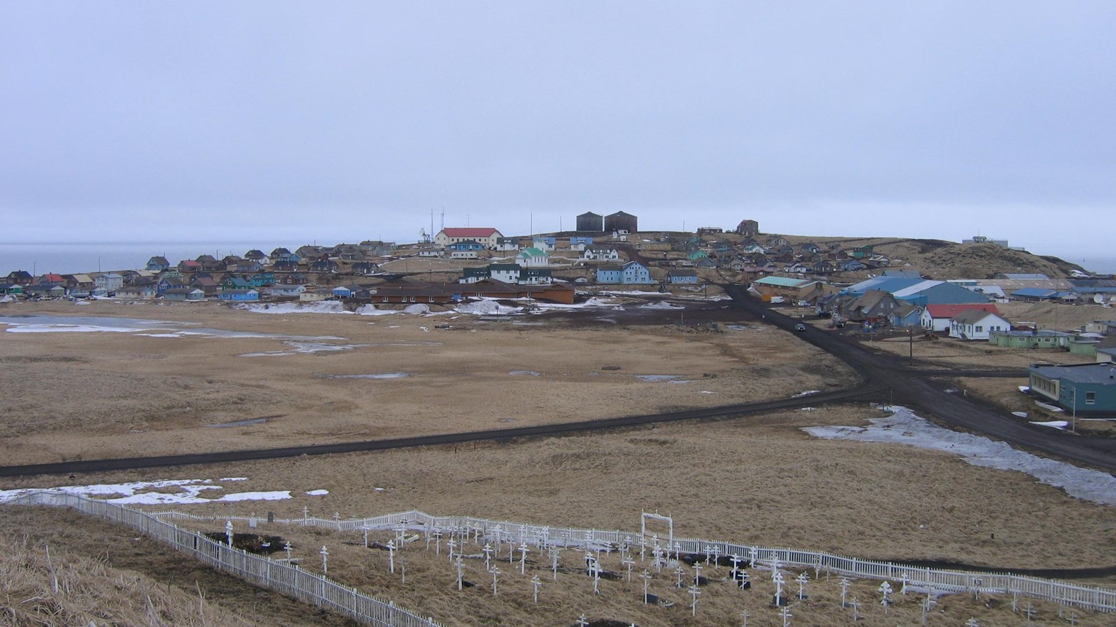A large historic village is on the horizon and white fenced Russian Orthodox cemetery in foreground