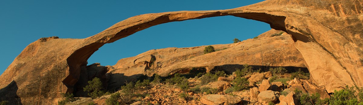 a broad, narrow arch with rock piles beneath and a blue sky above