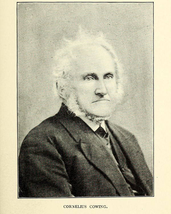 Portrait of an older man with white scruffy hair and beard sits in a dark suit.