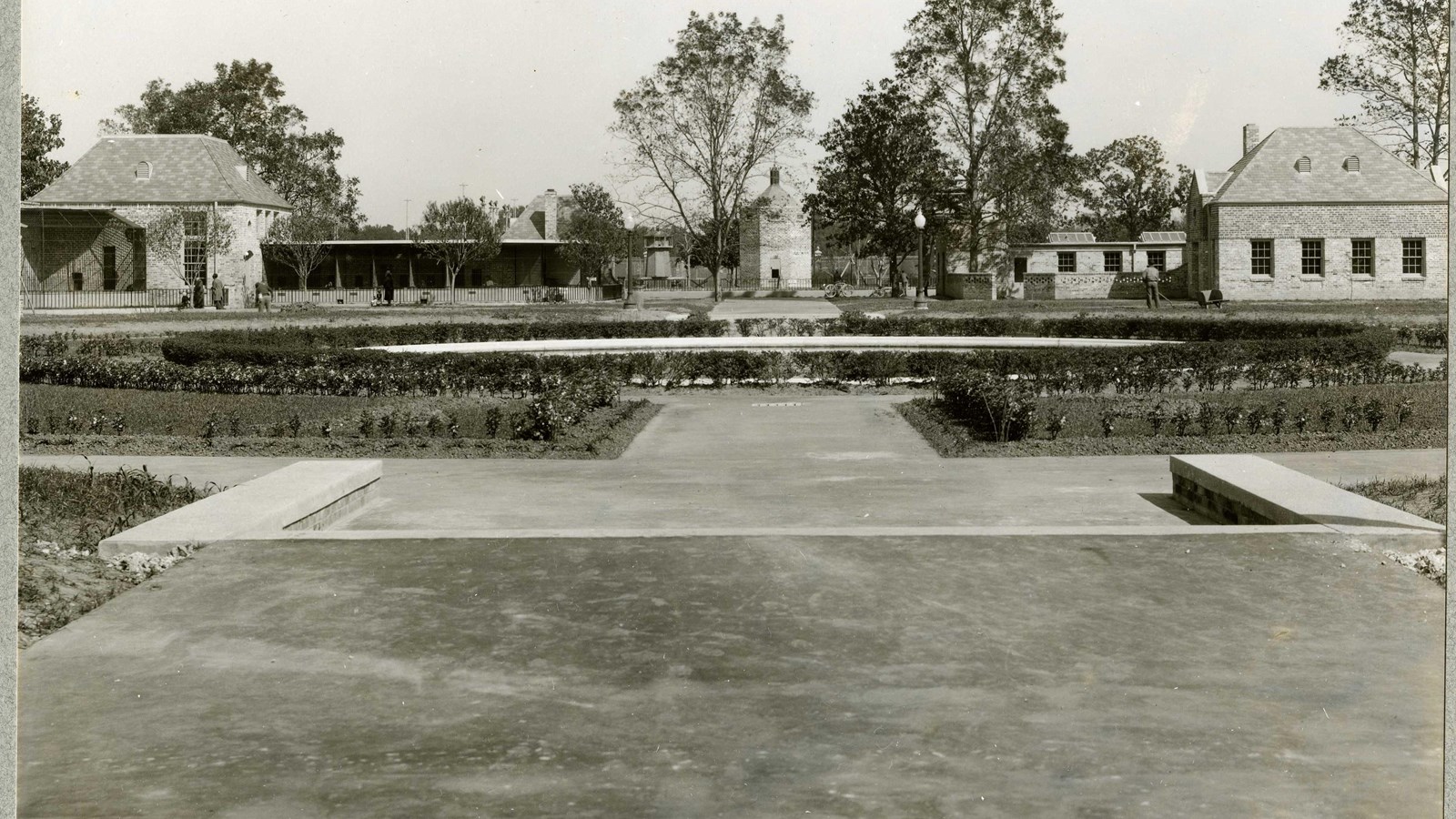 Black and white of flat area with trees and shrubs around a building. 