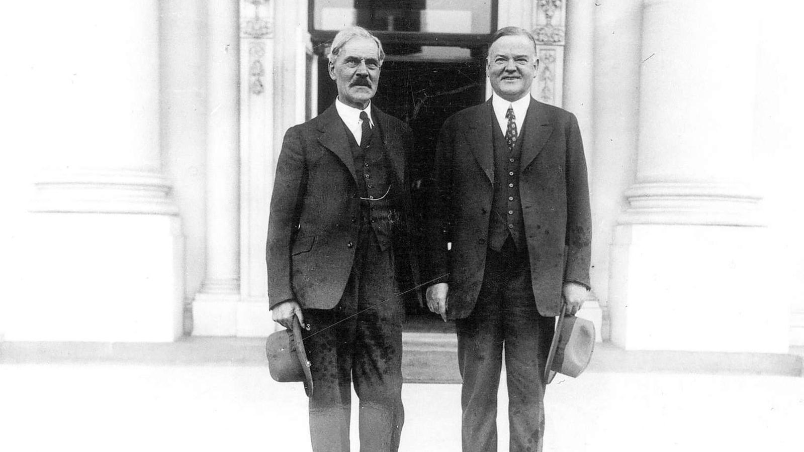 A black and white historic photo of two men in suits standing on steps of a large white building.
