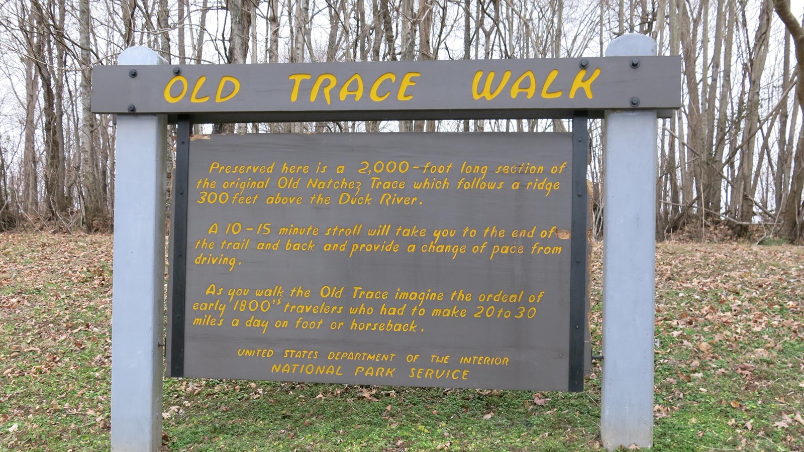 Wooden sign painted brown with yellow letters mentioning the short walk at that location