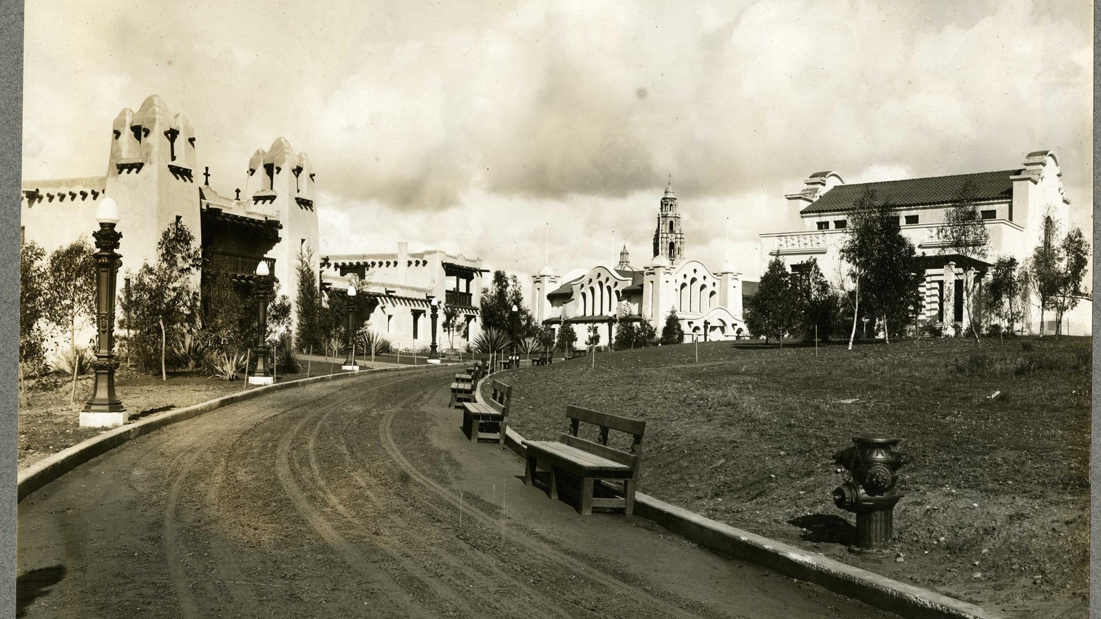 Black and white of dirt hill leading to buildings lined with benches. 