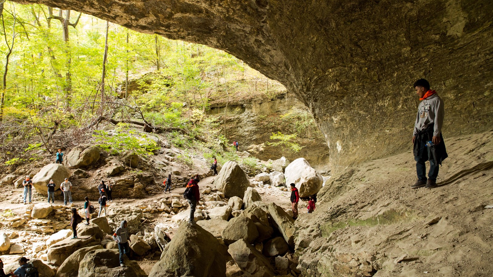 A hiker stands inside of a large bluff shelter, looking out at other hikers on the Lost Valley Trail