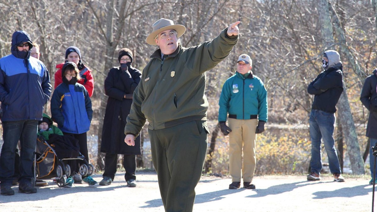 A park ranger standing with a crowd points to the landscape off camera.