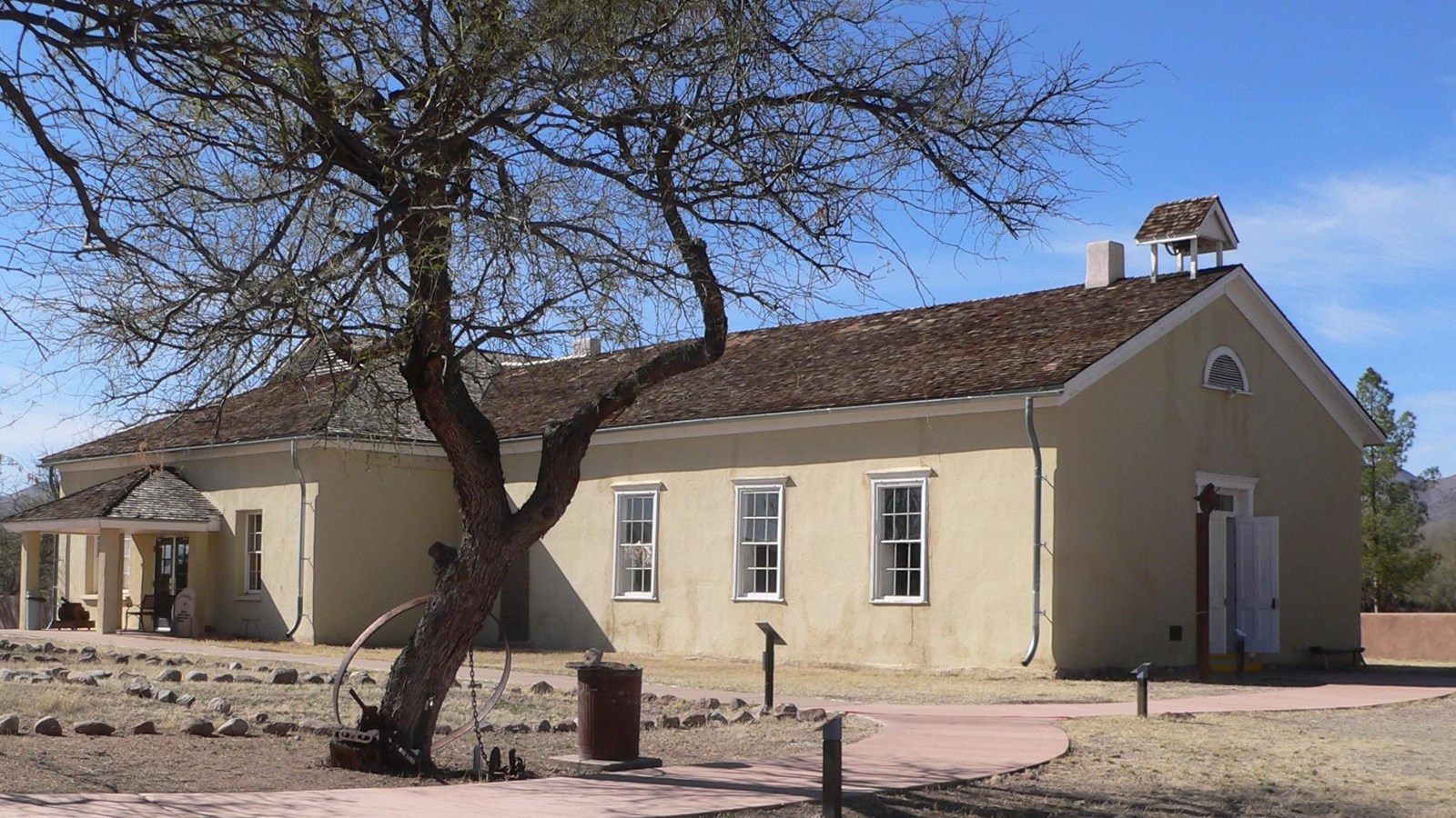 An old wagon frame in the foreground, with a historic adobe schoolhouse in the background