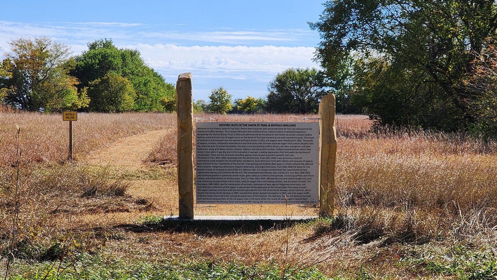 An interpretive panel about Santa Fe Trail ruts stands outside with brush and trees surrounding. 